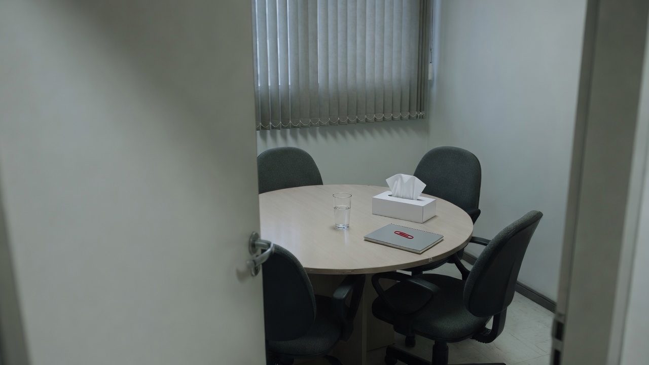 Sala de reunião pequena e fechada de uma empresa, com uma cadeira afastada da mesa